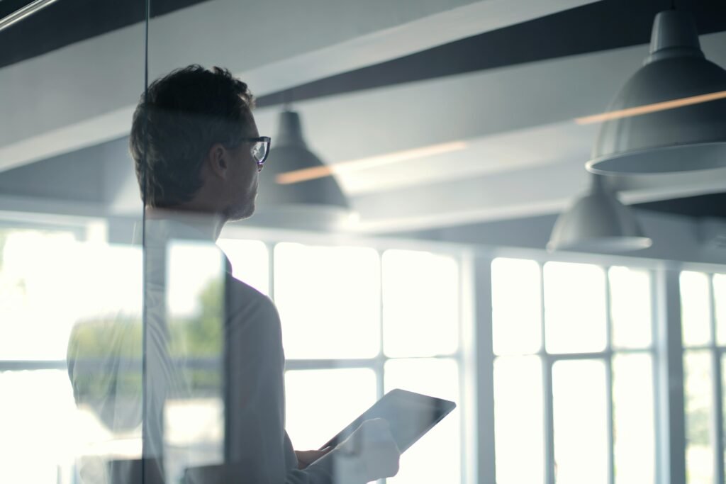 pexels-photo-3760093-3760093 A businessman holding a tablet in an office, looking thoughtfully through a glass wall.