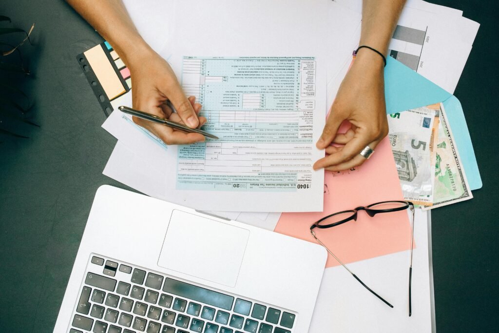 pexels-photo-8927687-8927687 Hands writing on tax documents with laptop, glasses, and currency on desk.